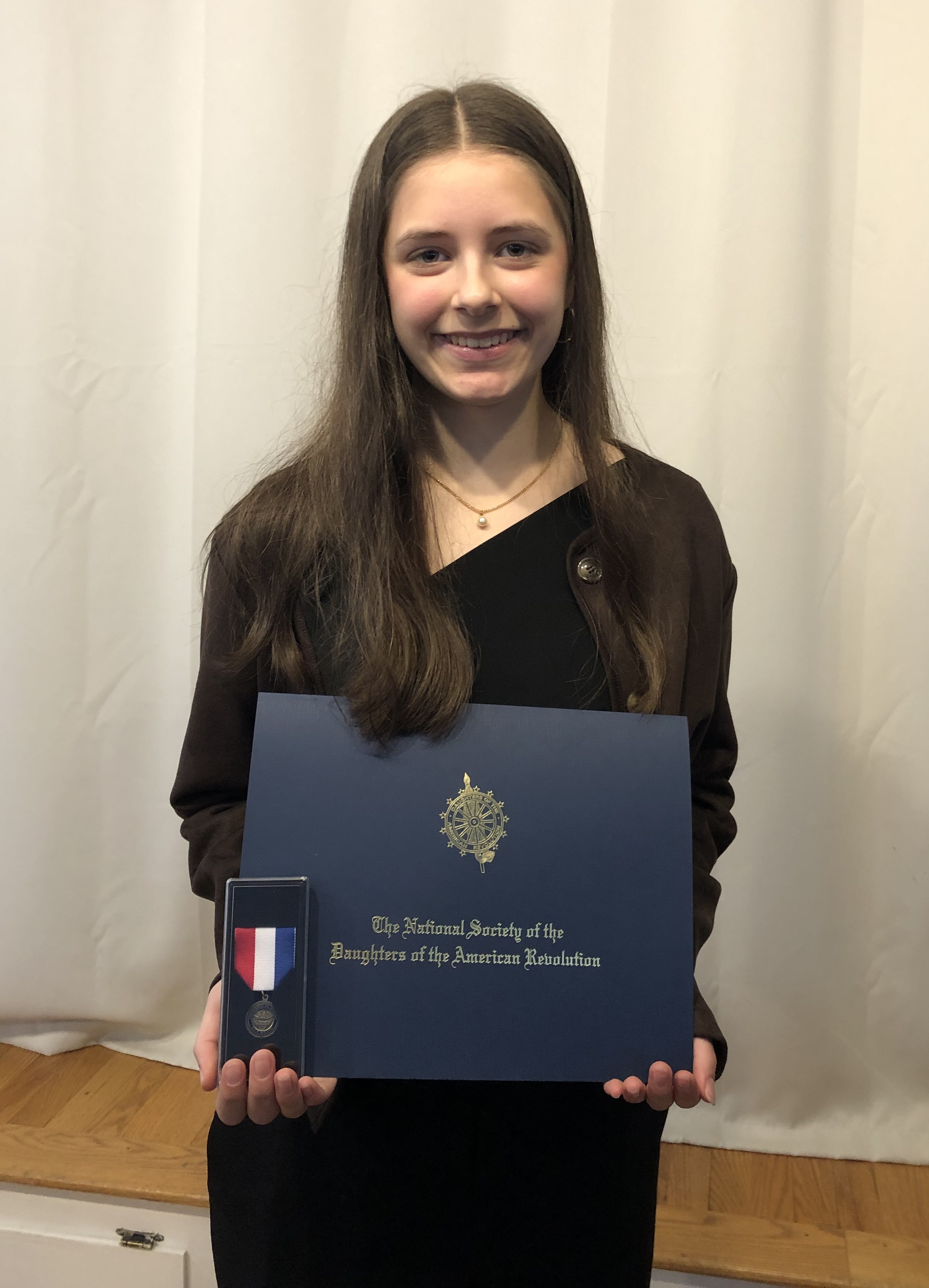 Lauren Daly holding a certificate with a medal from the National Society of the Daughters of the American Revolution.